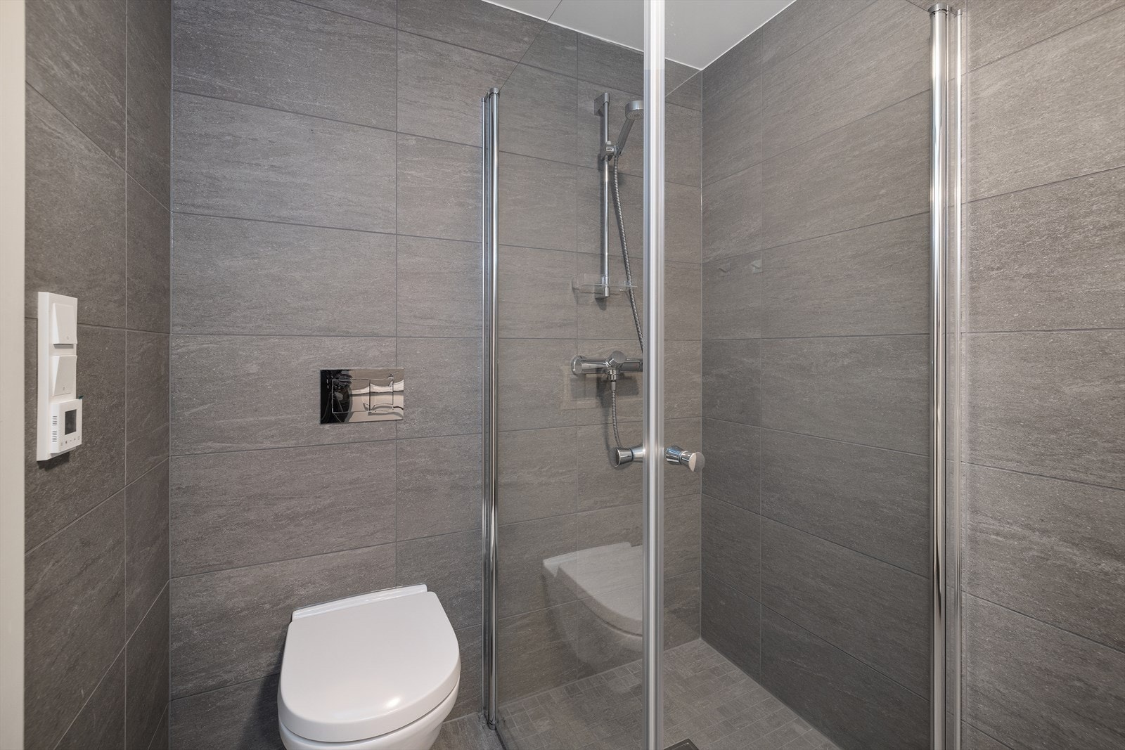 Badet er helfliset med vegghengt toalett og dusjhjørne med innfellbare glassdører. Galleribilde