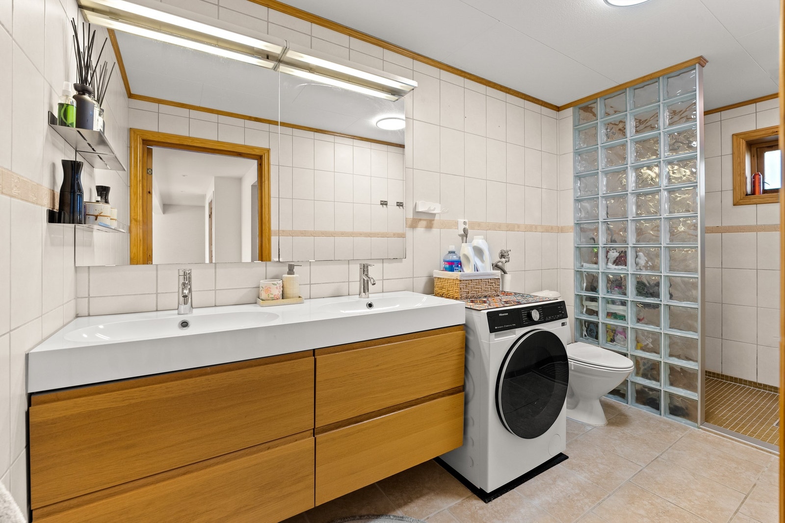 Dusjnisje med vegg av glassbyggerstein og dusjarmatur, og gulvmontert toalett. Det er opplegg for vaskemaskin. Galleribilde