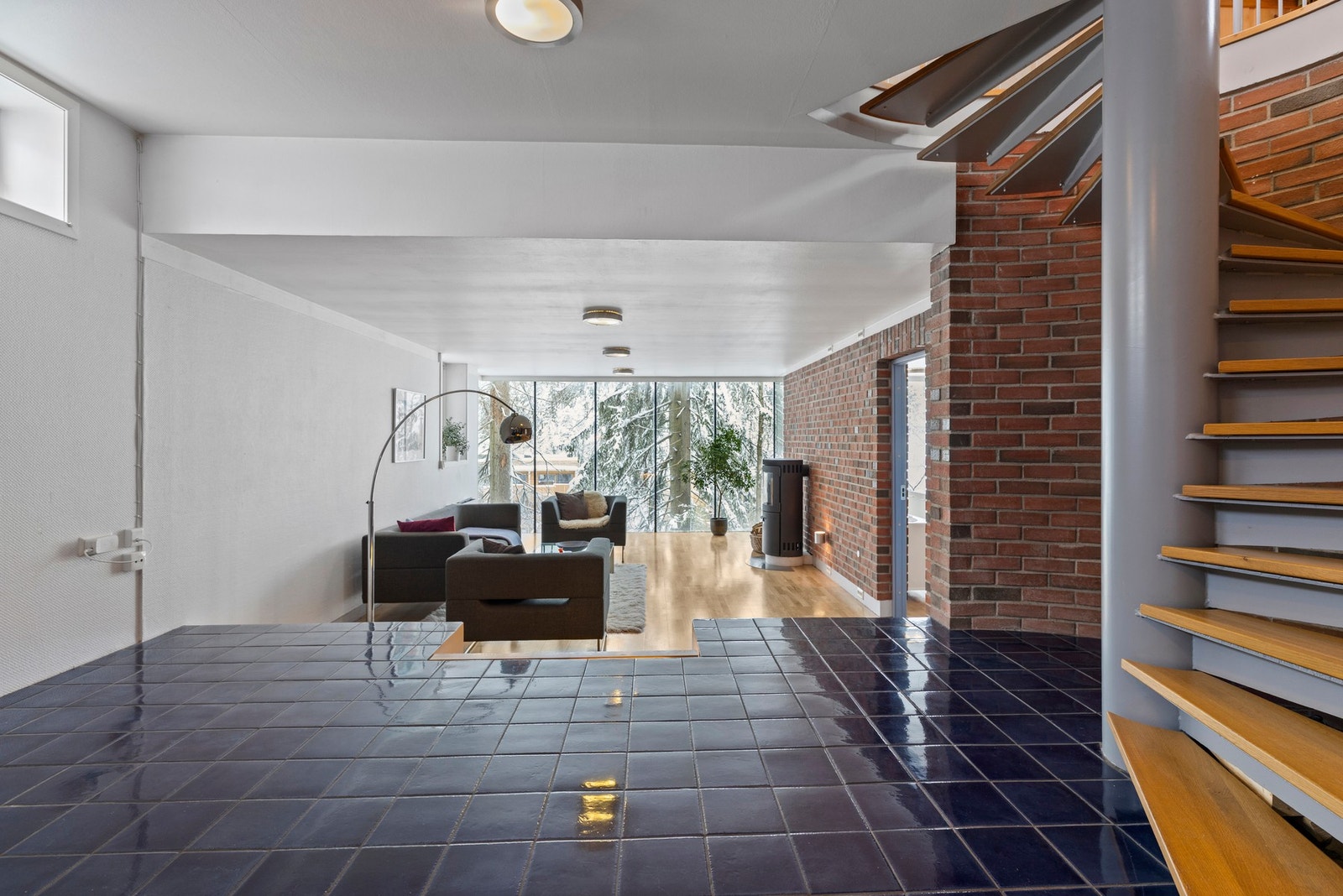 Romslig stue i underetasjen med store vindusflater og utsyn mot skog. Galleribilde