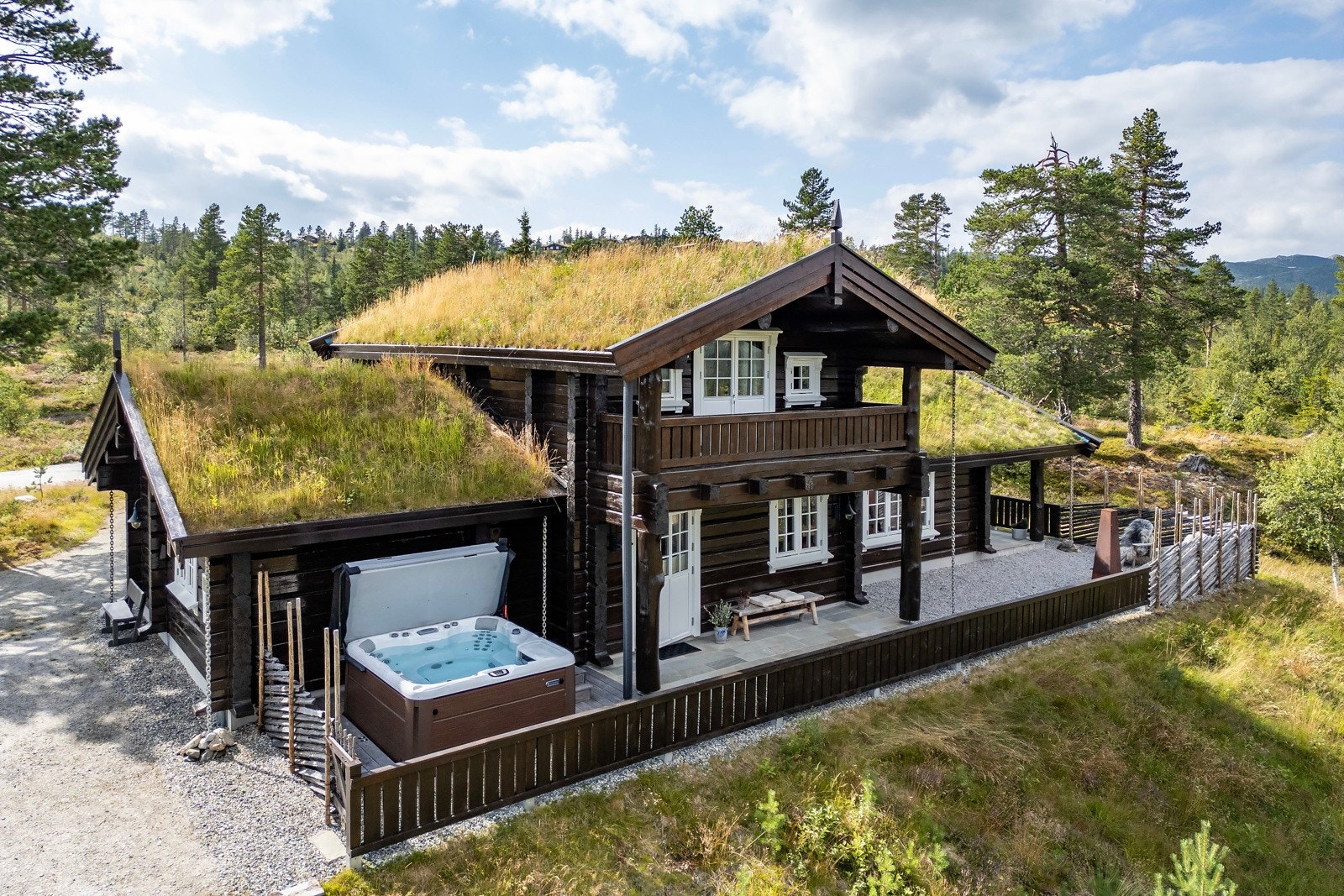 Tradisjonell tømmerhytte med torvtak, utendørs boblebad og terrasse, omgitt av skog og natur. Galleribilde