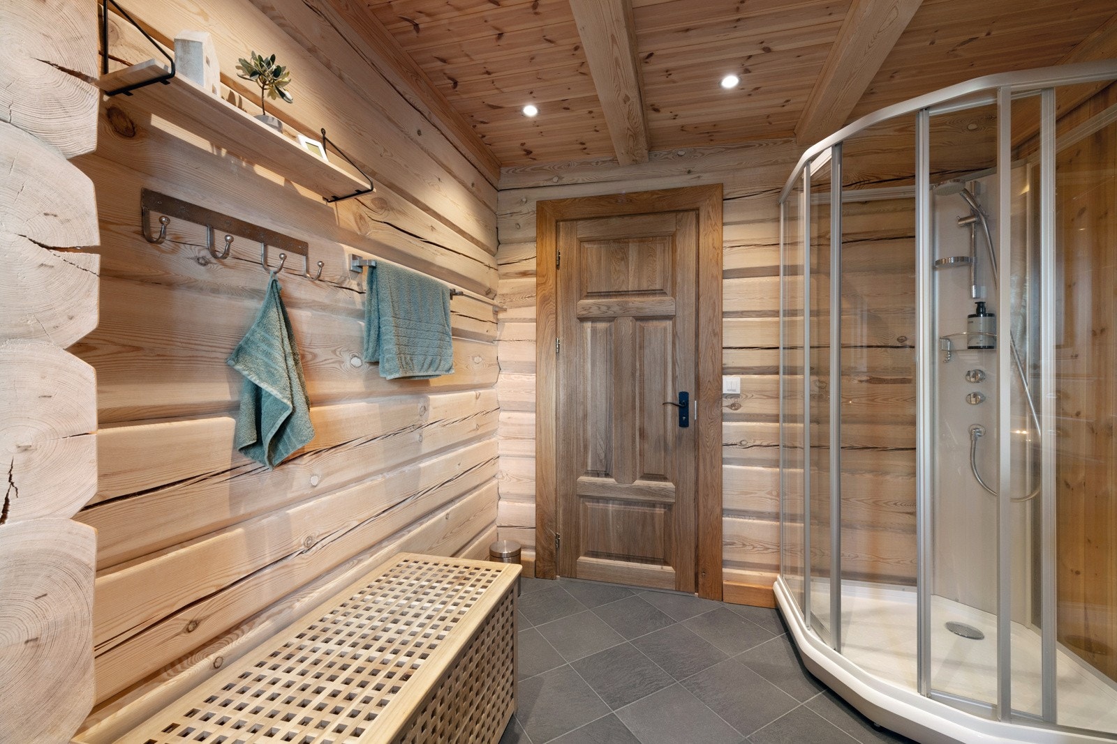 Bad med dusjkabinett, trepaneler og flislagt gulv. Vegghengt hylle og knagger. Galleribilde