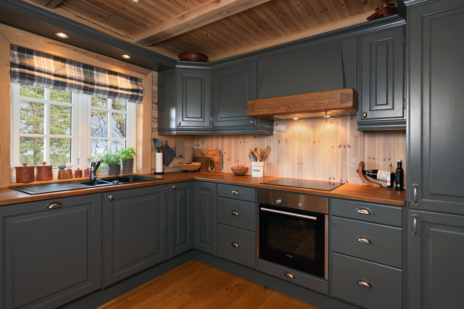Kjøkken med mørkegrå skap, treverk på vegger og tak, integrert komfyr og vindu med utsikt. Galleribilde
