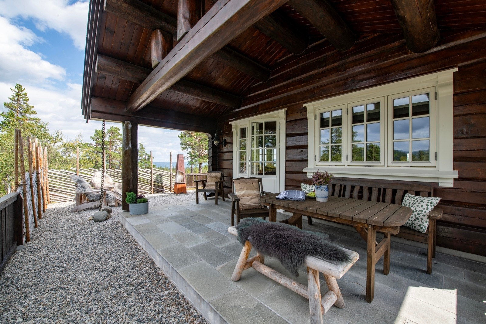 Koselig uteplass med overbygg, sittebenk, og bord. Gruslagt område med gode solforhold og utsikt til skog. Galleribilde