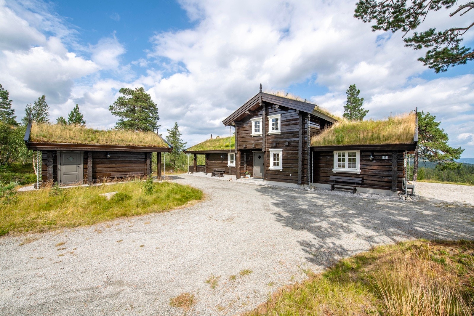 Tradisjonell hytte med torvtak, beliggende på en gruslagt tomt omringet av trær og natur Galleribilde