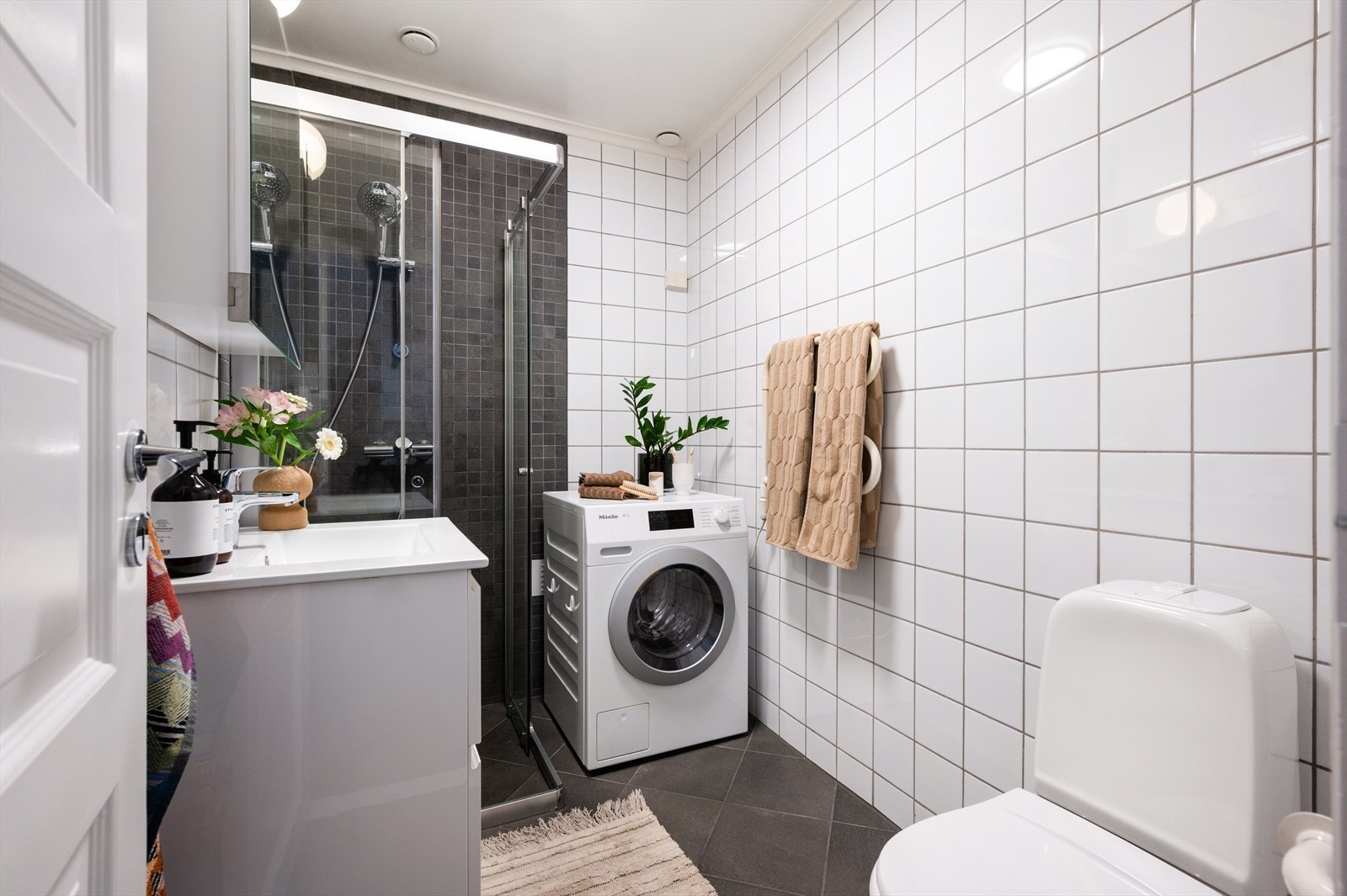 Flislagt bad med toalett, servant nedfelt i innredning og dusjhjørne med skyvedører. Galleribilde