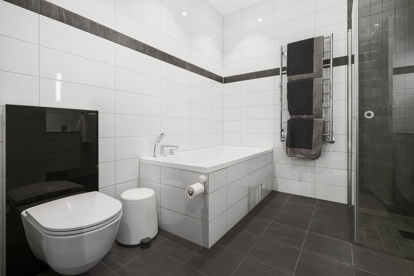 Rommet er innredet med badekar, dusjhjørne, servant med underskuffer, speil og vegghengt toalett. Galleribilde