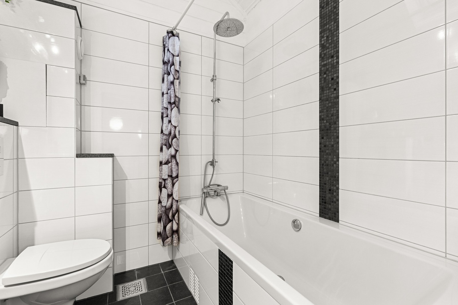 Baderomsinnredningen er bestående av plassbygget servant møbel med hyller i stein, toppmontert bolleservant, speil, vegghengt klosett og innfliset badekar med dusjgarnityr (regnfalldusj) Galleribilde