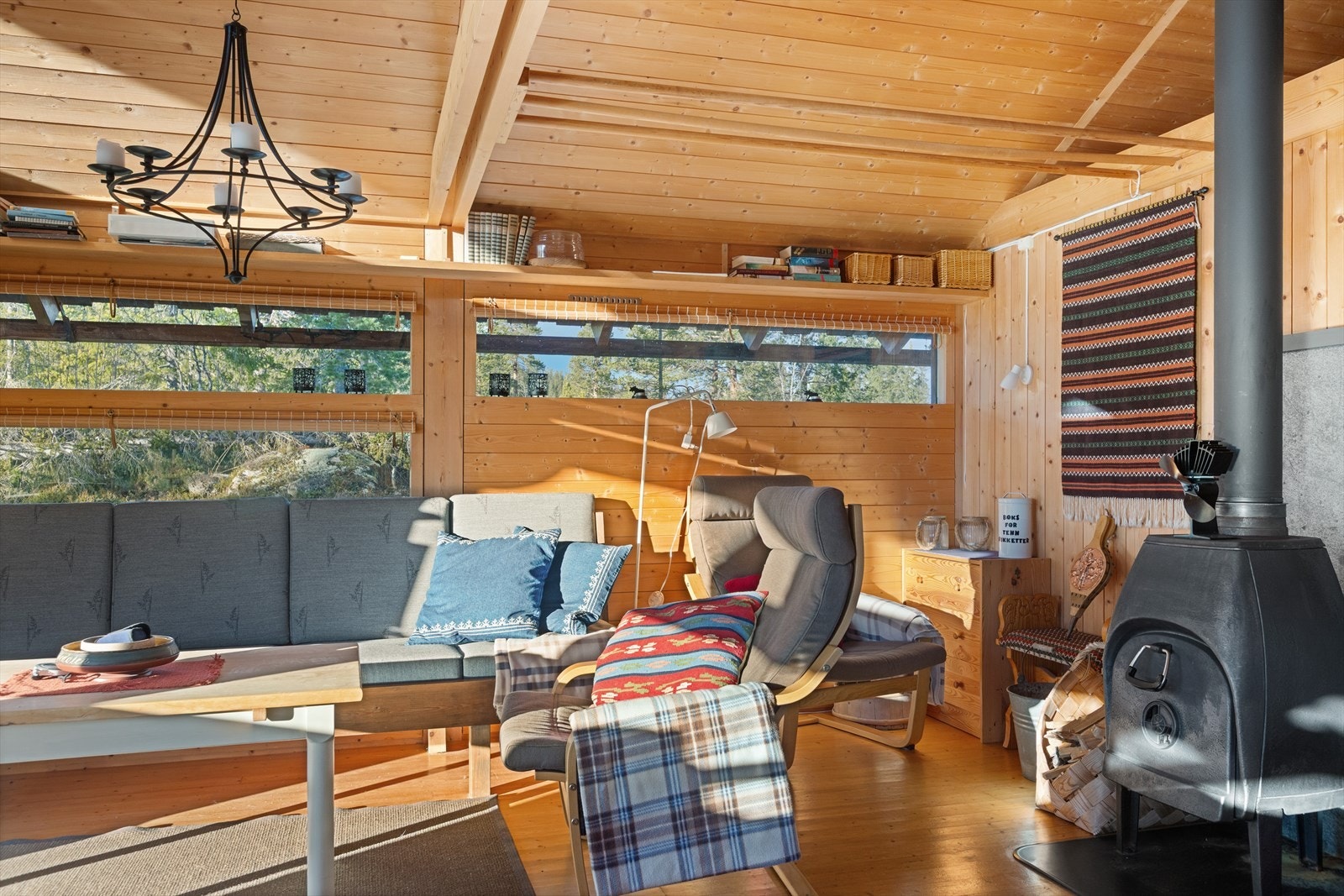 Den åpne løsningen mellom stue og kjøkken gir fin plass til både sofa- og spisegruppe. En større peisovn med stålpipe gir rask og god oppvarming til hytta. Galleribilde