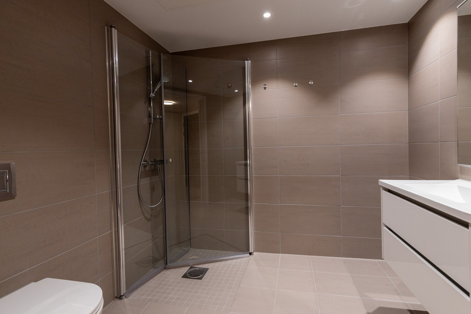 Dette stilrene baderommet byr på en hyggelig atmosfære med flislagt gulv og behagelig vannbåren varme, flislagte vegger og malte himlingsplater med innfelte spotter. Galleribilde