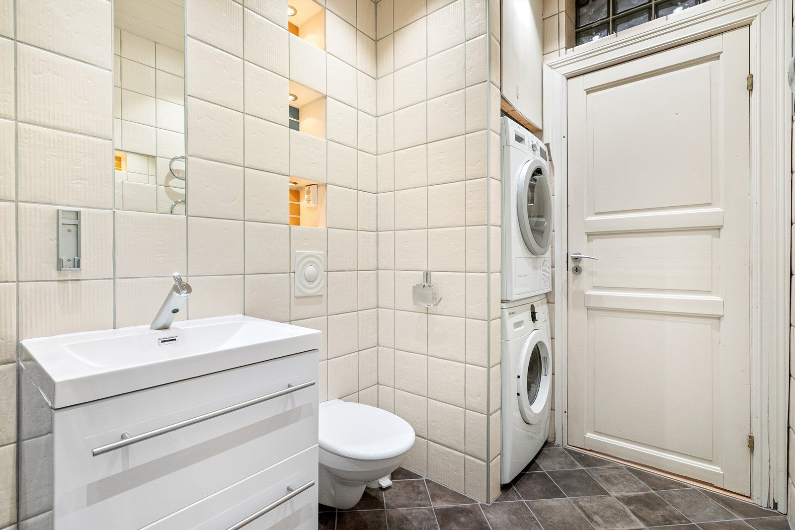 Badet er utstyrt med dusjhjørne med blandebatteri, regndusj og håndholdt slange, veggmontert toalett og baderomsinnredning med skuffer, hvit servant og blandebatteri. Galleribilde