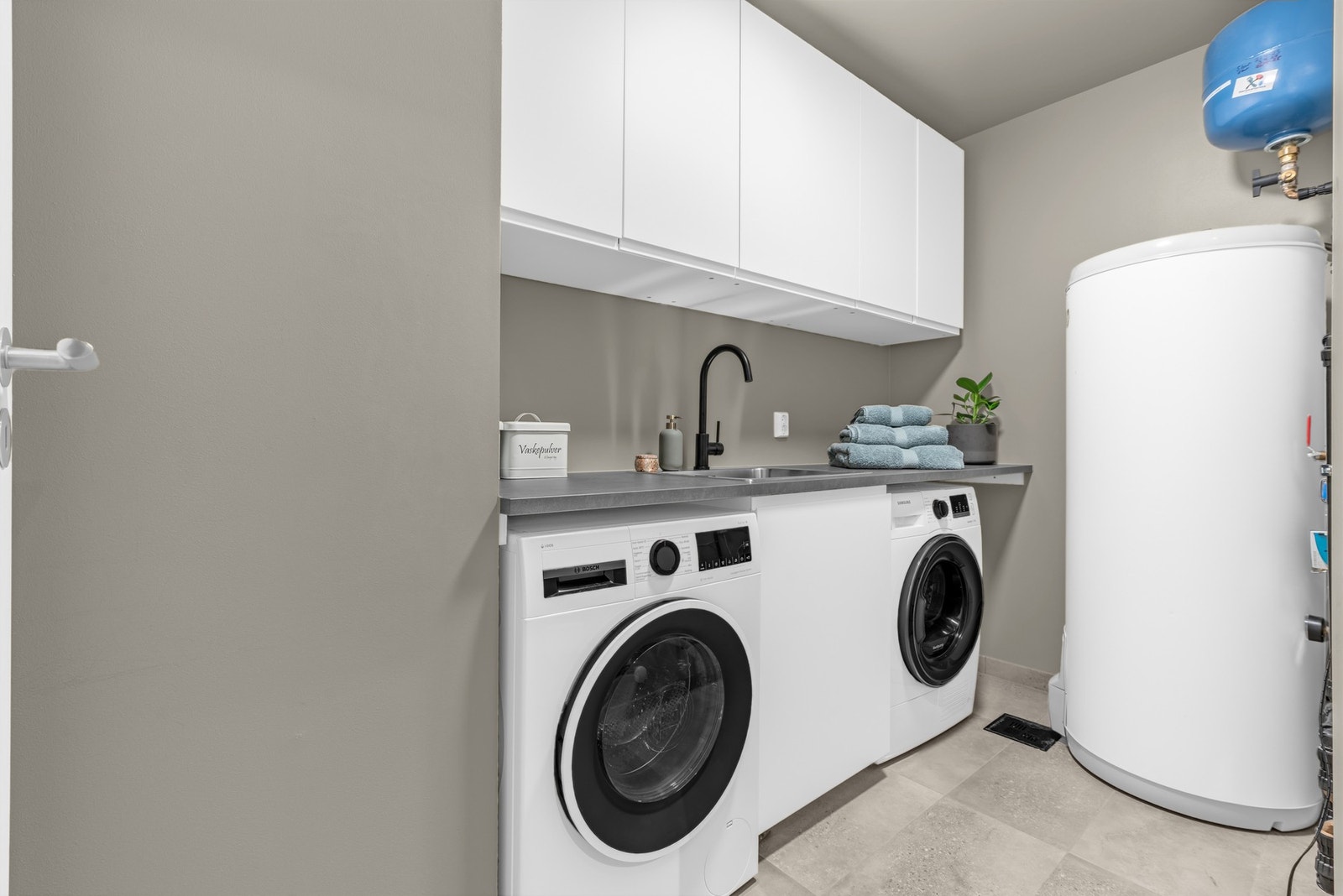 Boligen har et separat vaskerom med flislagt gulv med varmekabler. Her er det opplegg for både vaskemaskin og tørketrommel Galleribilde