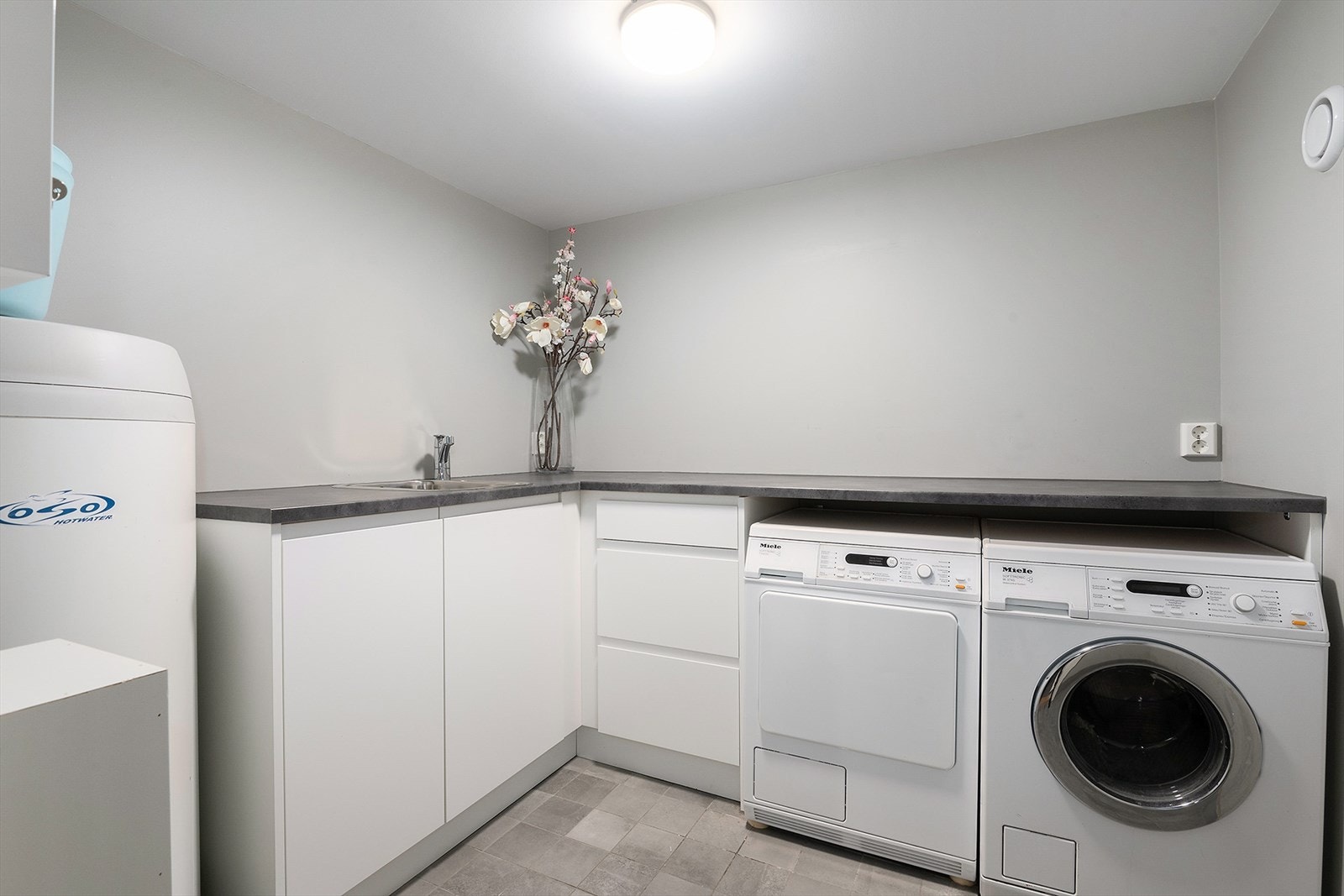 Boligen har eget vaskerom med utslagsvask, godt med skap- og benkeplass og opplegg for vaskemaskin og tørketrommel under praktisk benk. Galleribilde