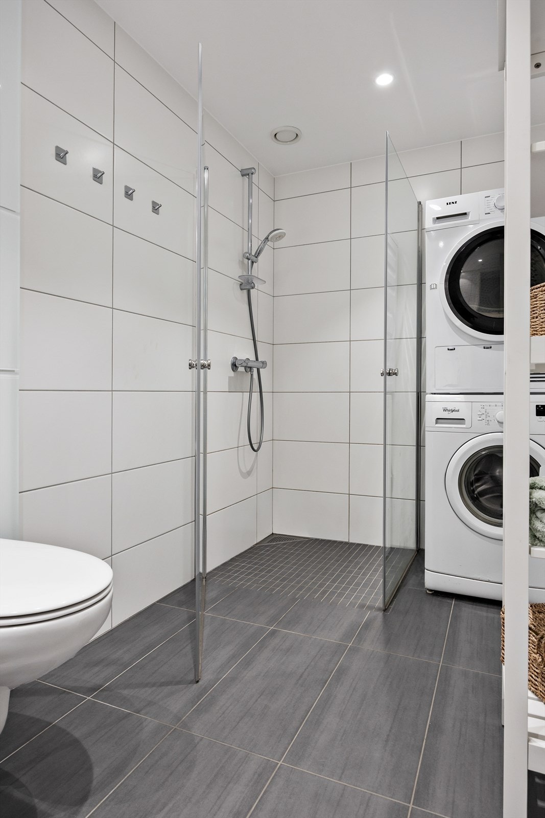 Innredningen består av vegghengt toalett, servant med underskap, speil, dusjnisje med innfellbare glassvegger, og en praktisk vaskesøyle i hjørne Galleribilde