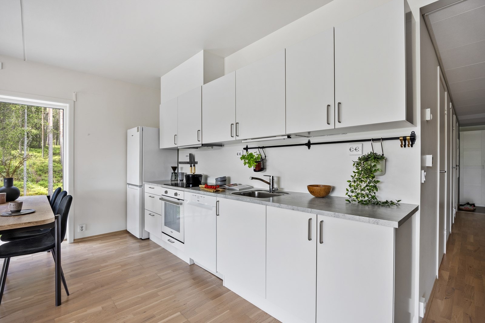 Kjøkkeninnredningen har hvite glatte skapfronter, laminert benkeplate med oppvaskkum, og integrert stekeovn og koketopp Galleribilde