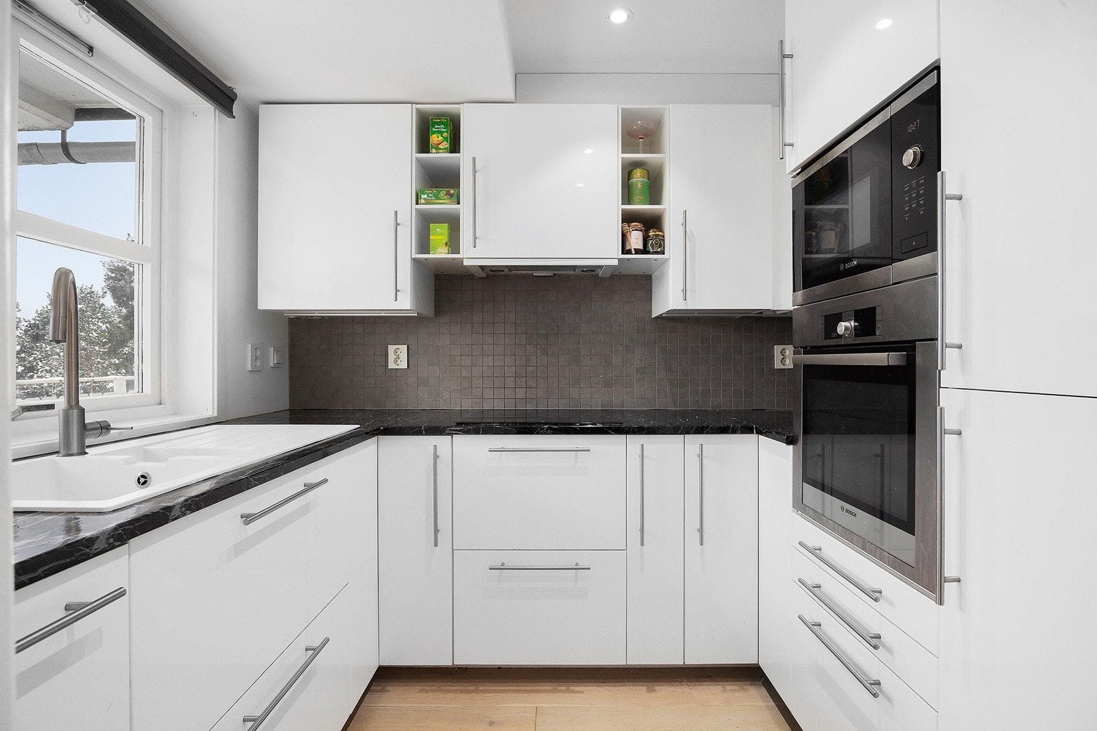 Kjøkkeninnredning med glatte høyglans skapfronter, heltre benkeplate belagt med folie, flislagt bakvegg, 1 1/2 oppvaskkum med beslag, ventilator og innfelte hvitevarer som koketopp, stekeovn, mikrobølgeovn, oppvaskmaskin, kjøl/- fryseskap. Galleribilde