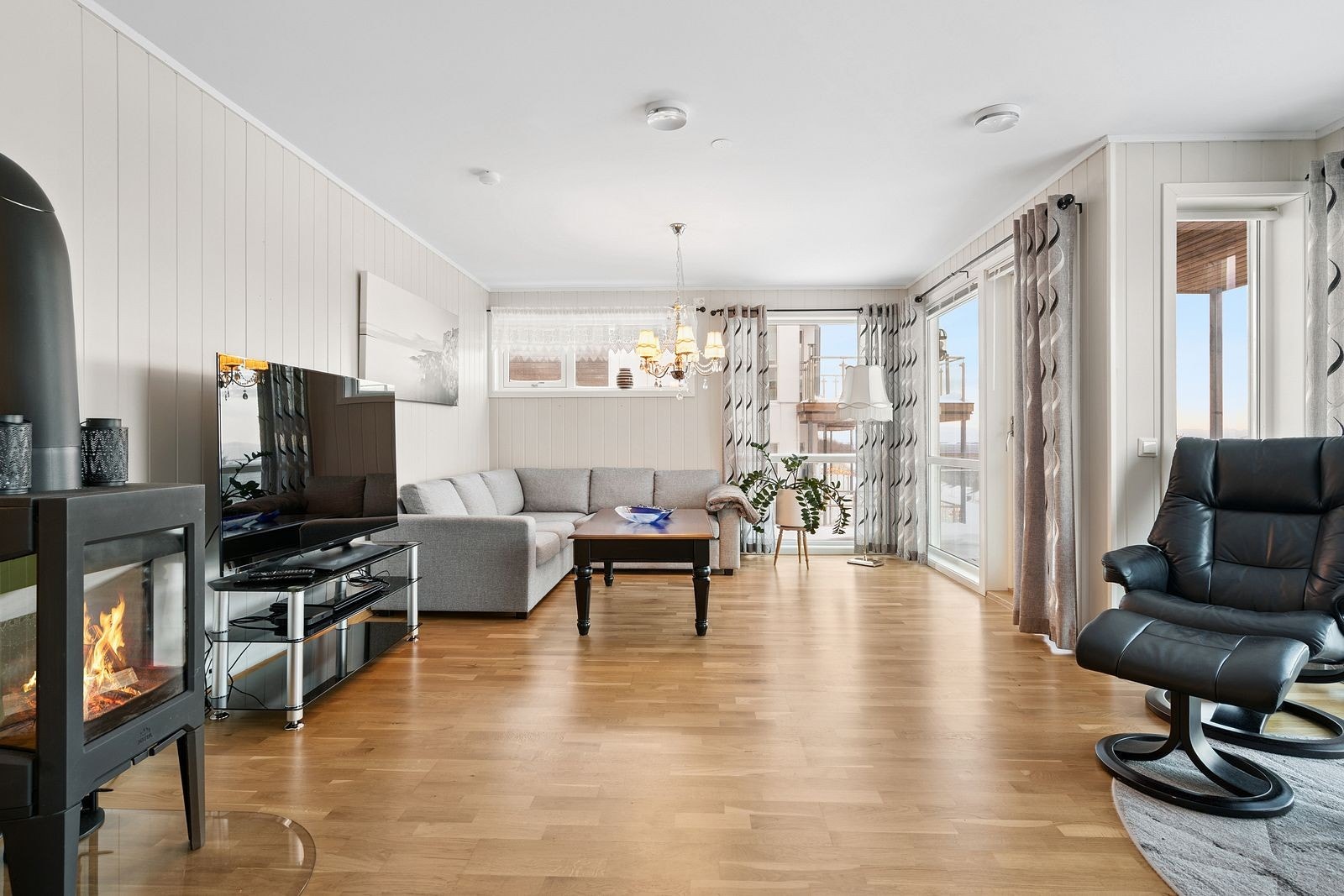 Vedovn og varmepumpe gir effektiv oppvarming når planløsningen har åpen løsning mellom stue, kjøkken og gang. Det er en vinkel inn i bygningsmassen ved terrassen slik at man kan få litt ly for Nordavinden. Galleribilde