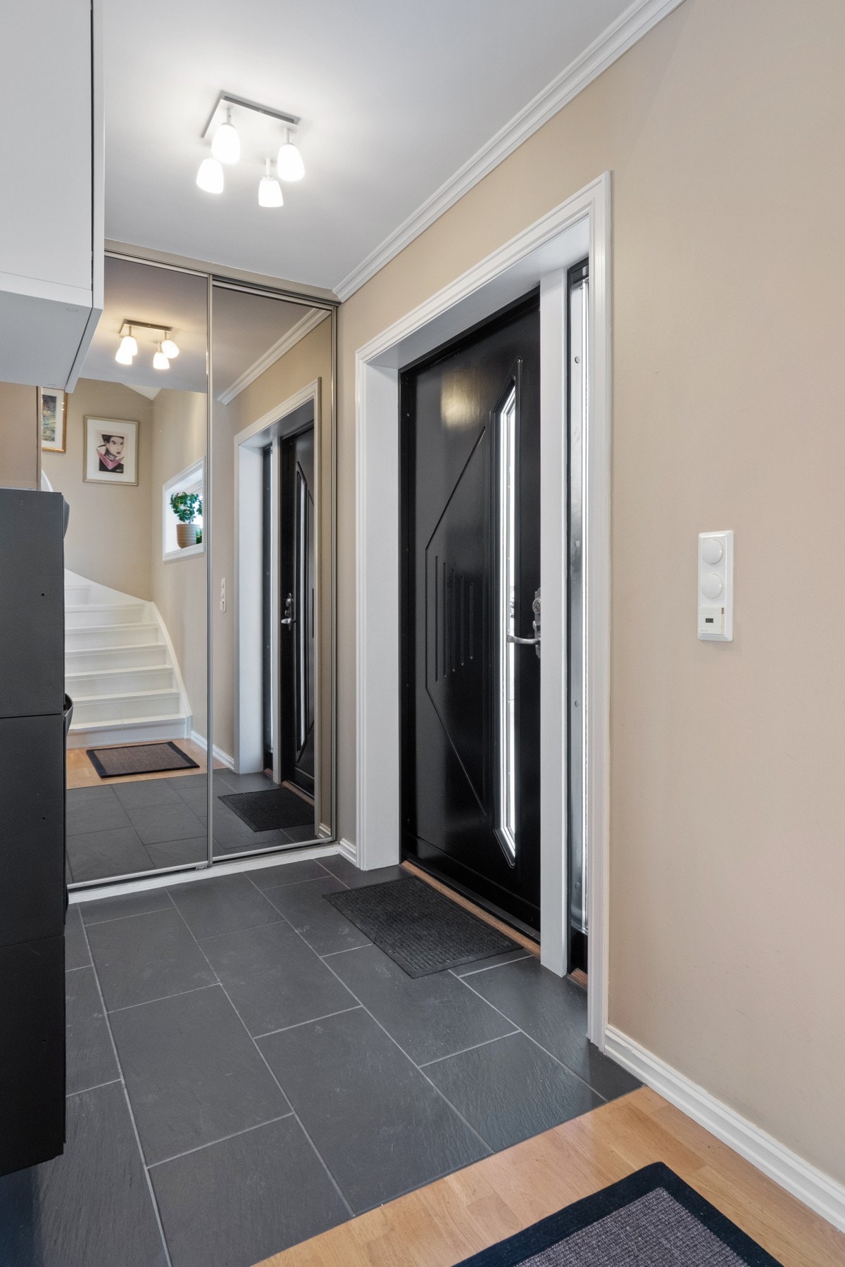 Praktisk entré med kombinasjon av parkett og store, sorte gulvfliser. Det er varmekabler under flisene, og yttertøy og sko kan ryddes enkelt bort i en plassbygd skyvedørsgarderobe med speilfronter. Galleribilde