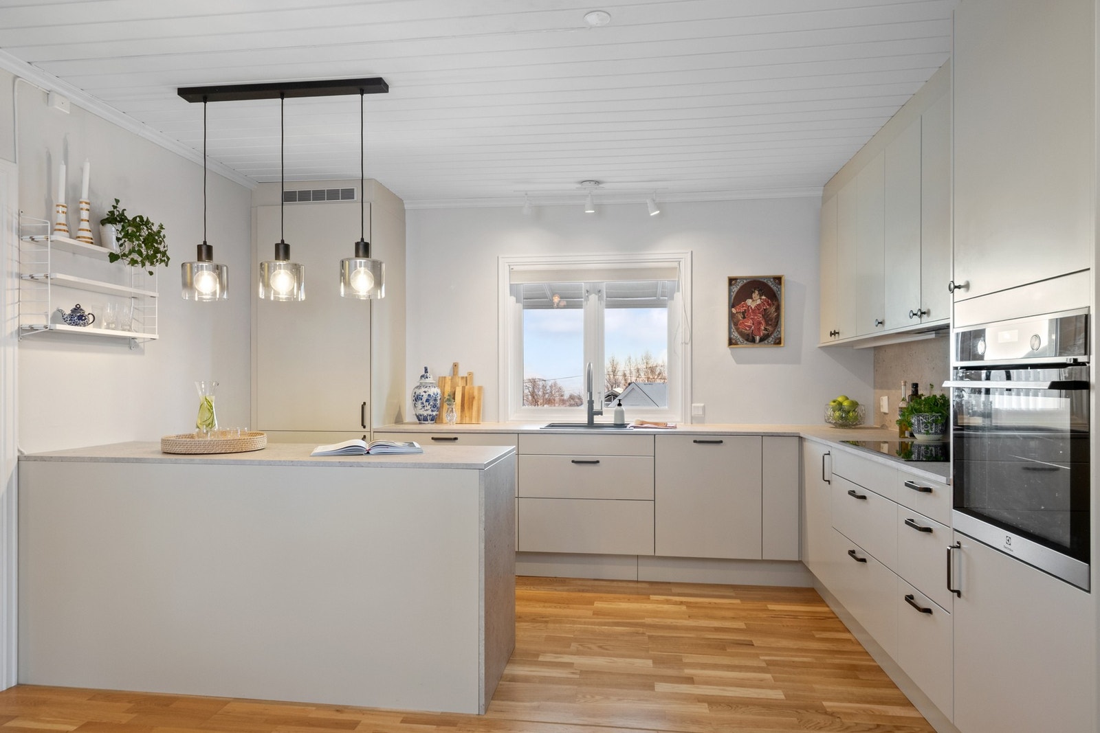 Innredningen fremstår moderne og elegant, med glatte, lysegrå fronter, laminert benkeplate, sort oppvaskkum i kompositt og Quooker-kran med kokende vann. Galleribilde