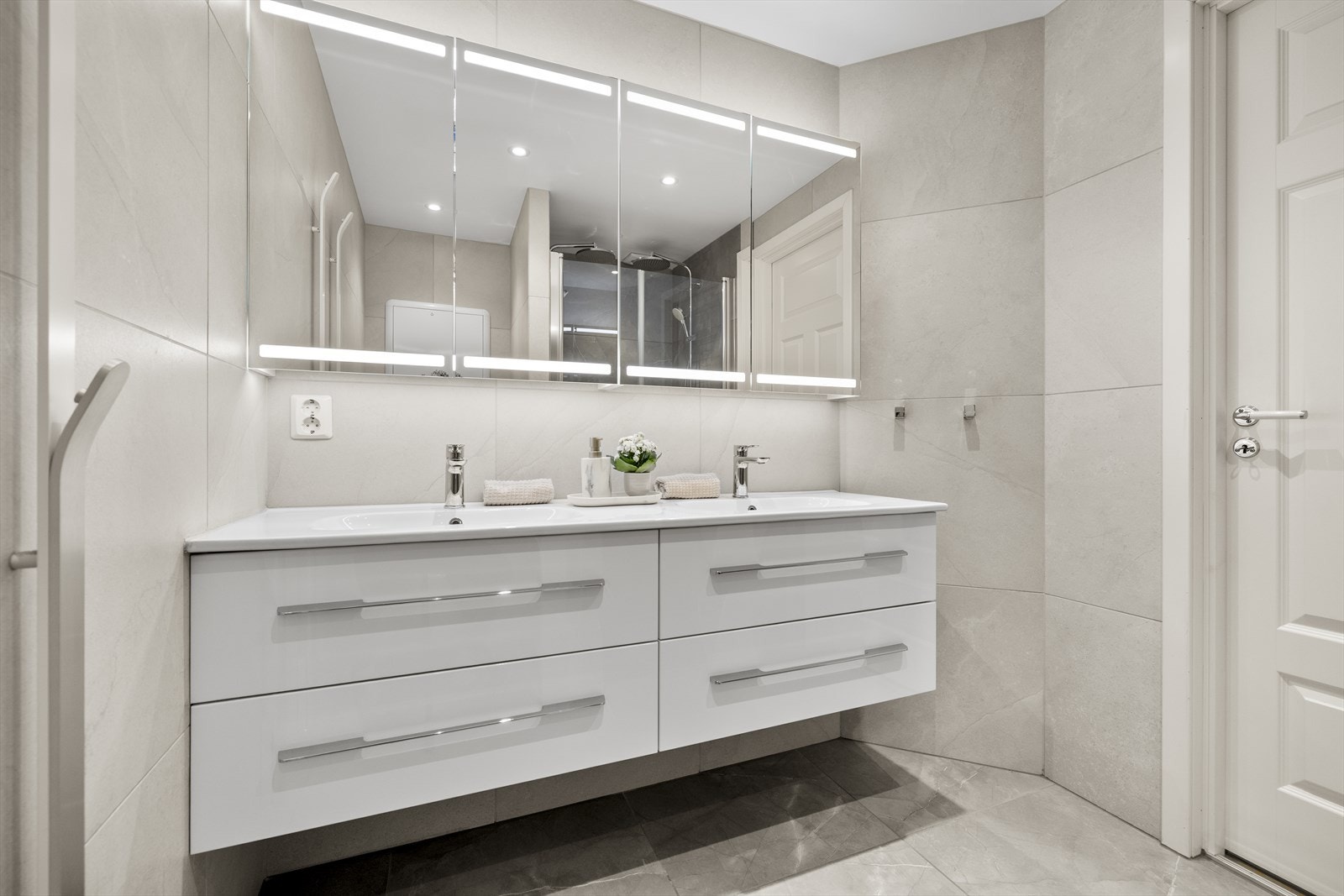 Badet innehar vegghengt toalett, dobbelservant med skuffer og dusjnisje med dobbeldusj og glassdører. Galleribilde