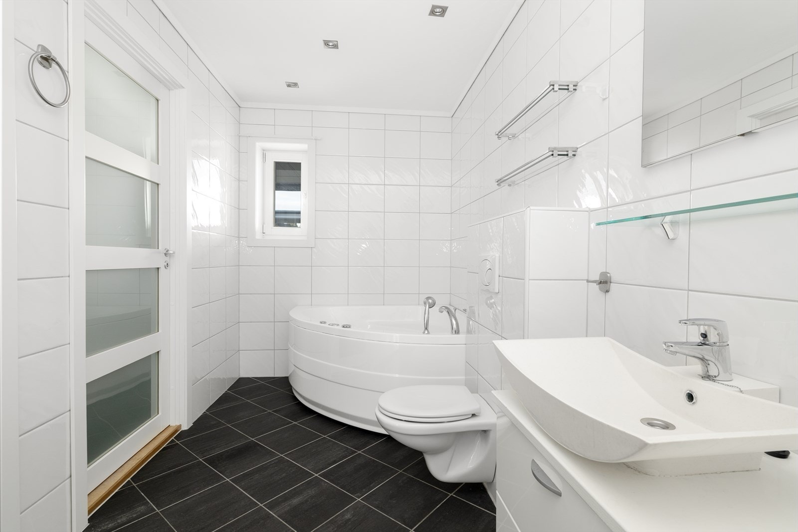 Badet inneholder dobbel servant med underskap, hyller og speil med lys over, dusjkabinett, badekar og vegghengt toalett. Galleribilde