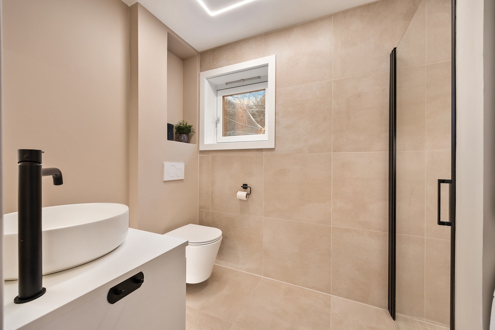 Her er det veggfestet klosett med innebygget sisterne og en dusjnisje med dør i herdet glass Galleribilde