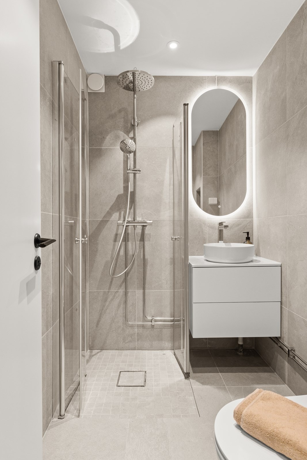 Badet har delikate detaljer bestående av adskilt dusjsone med to skyvbare foldedører, vegghengt wc med innebygd sisterne, servant med underliggende innredning, speil med integrerte lys og varmekabler i gulv. Galleribilde