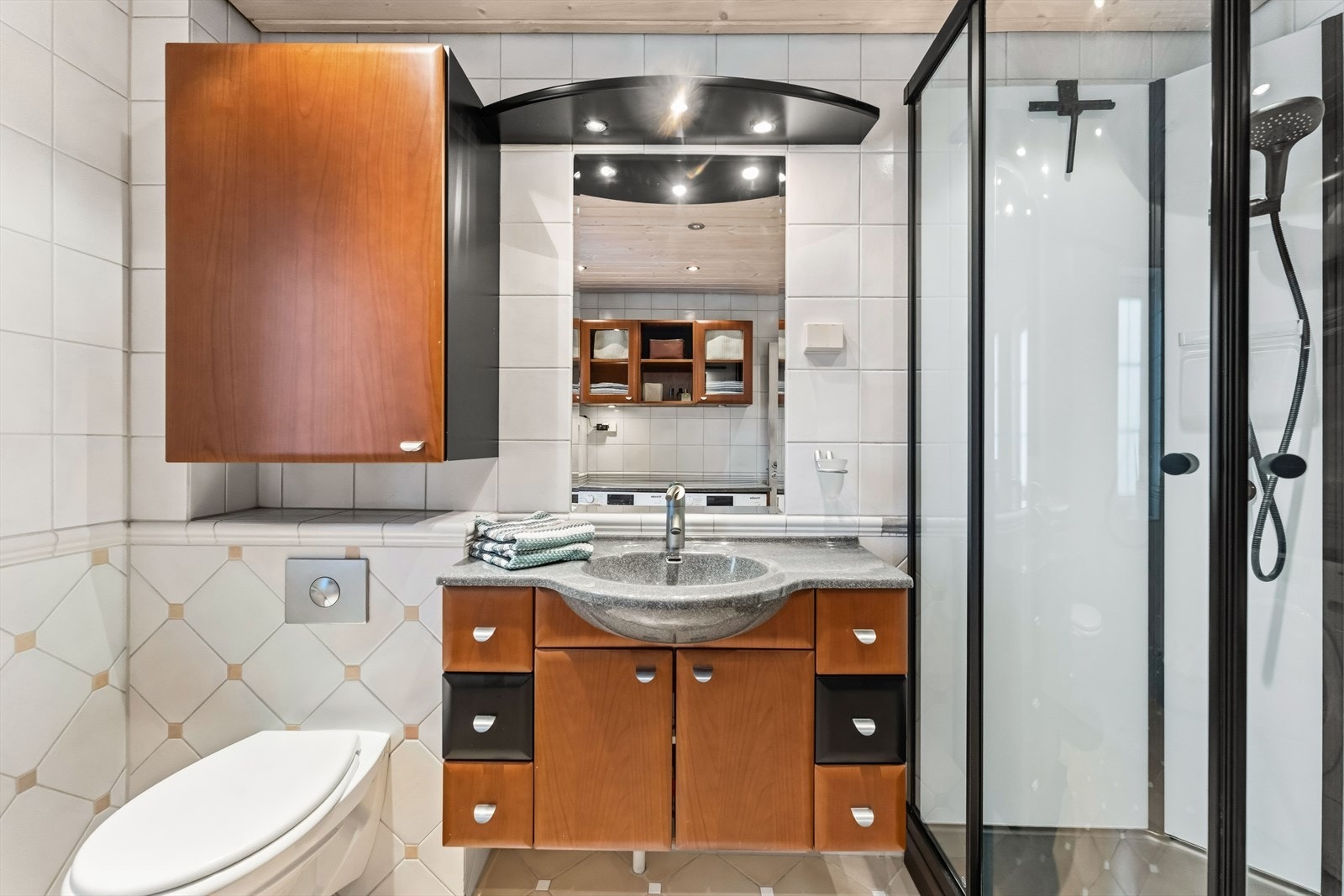 Innredningen er kirsebærfarget og består av servantinnredning, flere veggskap, hylle samt speil med overlys. Galleribilde