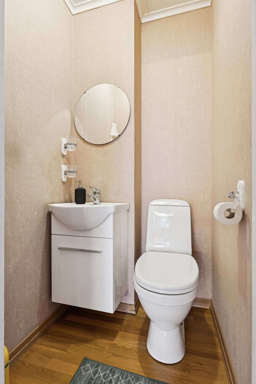 Toalettrommet har parkettgulv og tapetserte vegger, samt en keramisk vaskeservant med benkskap. Galleribilde