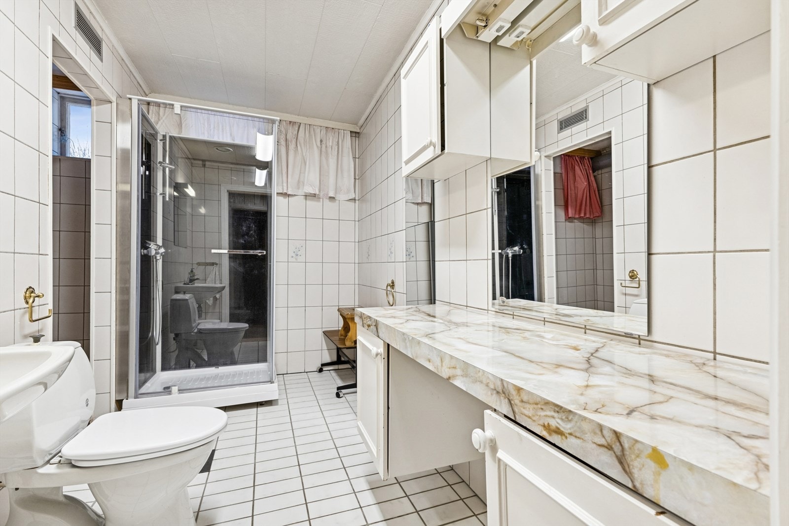 Flislagte overflater og stor benkeplate gir funksjonelt bad. Det er tilknyttet ventilasjonsanlegg, men badet er modent for full restaurering. Galleribilde