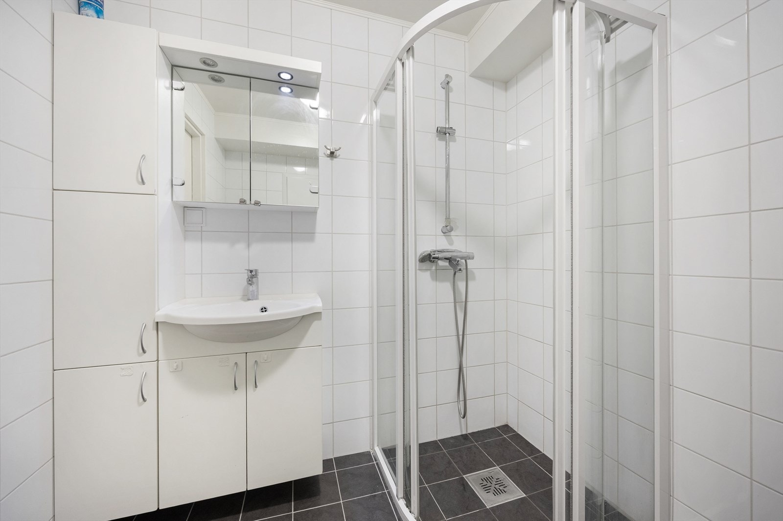 Baderomsinnredning med servant, speilskap og et praktisk høyskap for ekstra oppbevaring. Galleribilde