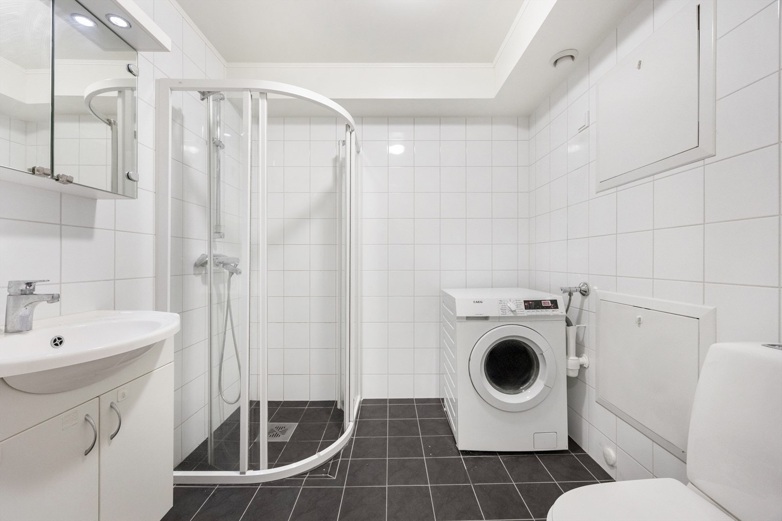 Helfliset bad med dusjhjørne med innfellbare glassdører og opplegg for vaskemaskin. Galleribilde