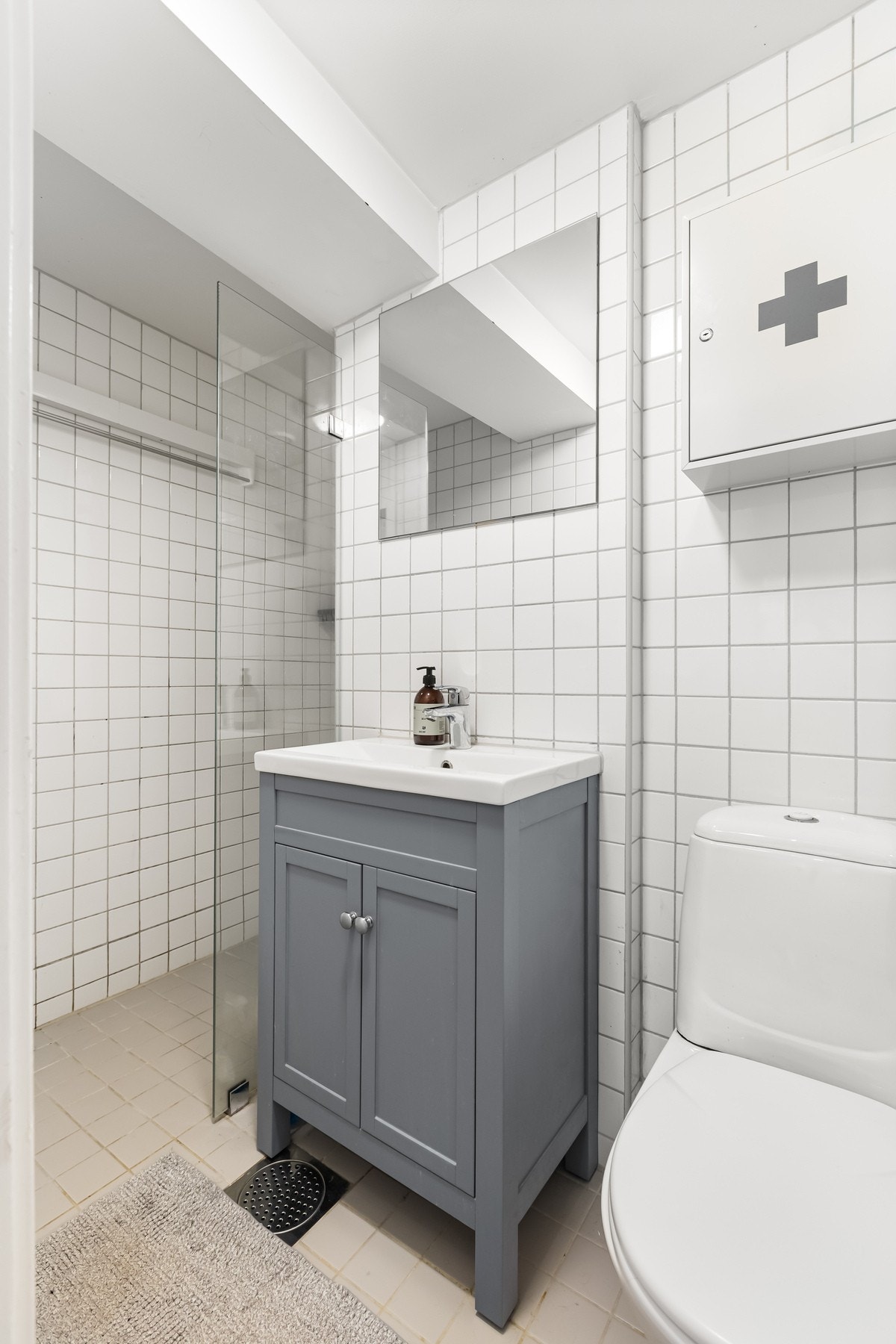 Baderom fra 2005 med tidløse fliser og pen innredning. Badet består av gulvmontert toalett, dusjhjørne med fastmontert dusjvegg, skapinnredning med nedfelt, heldekkende servant og opplegg for vaskemaskin og tørketrommel. Galleribilde