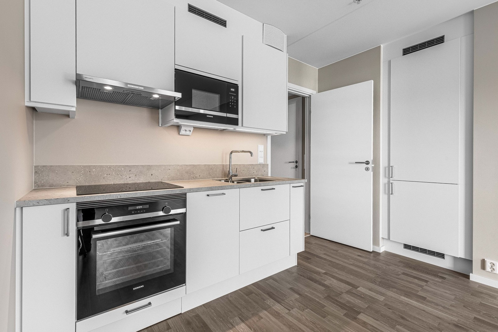 Innredningen har hvite, glatte fronter, takoppforede skap og lysegrå laminatbenkeplate med planlimt kum i stål. Galleribilde