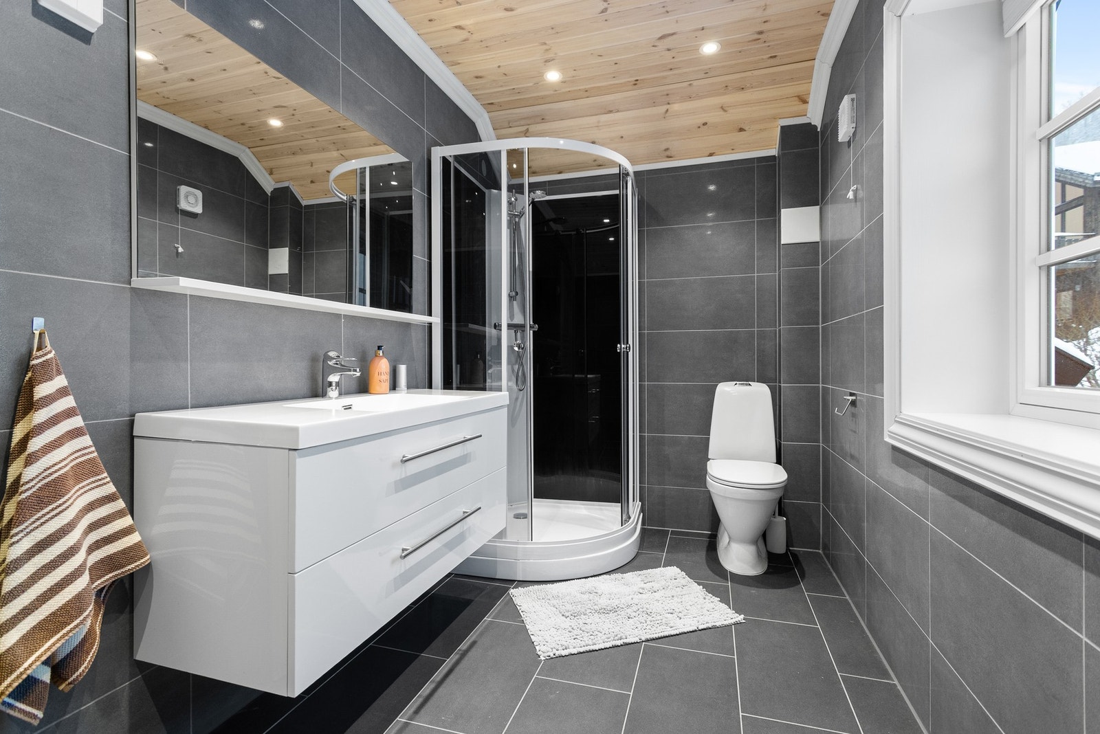 Flislagt baderom med toalett, innredning med servant og dusjkabinett. Varmekabler i gulv og downlights i himling Galleribilde