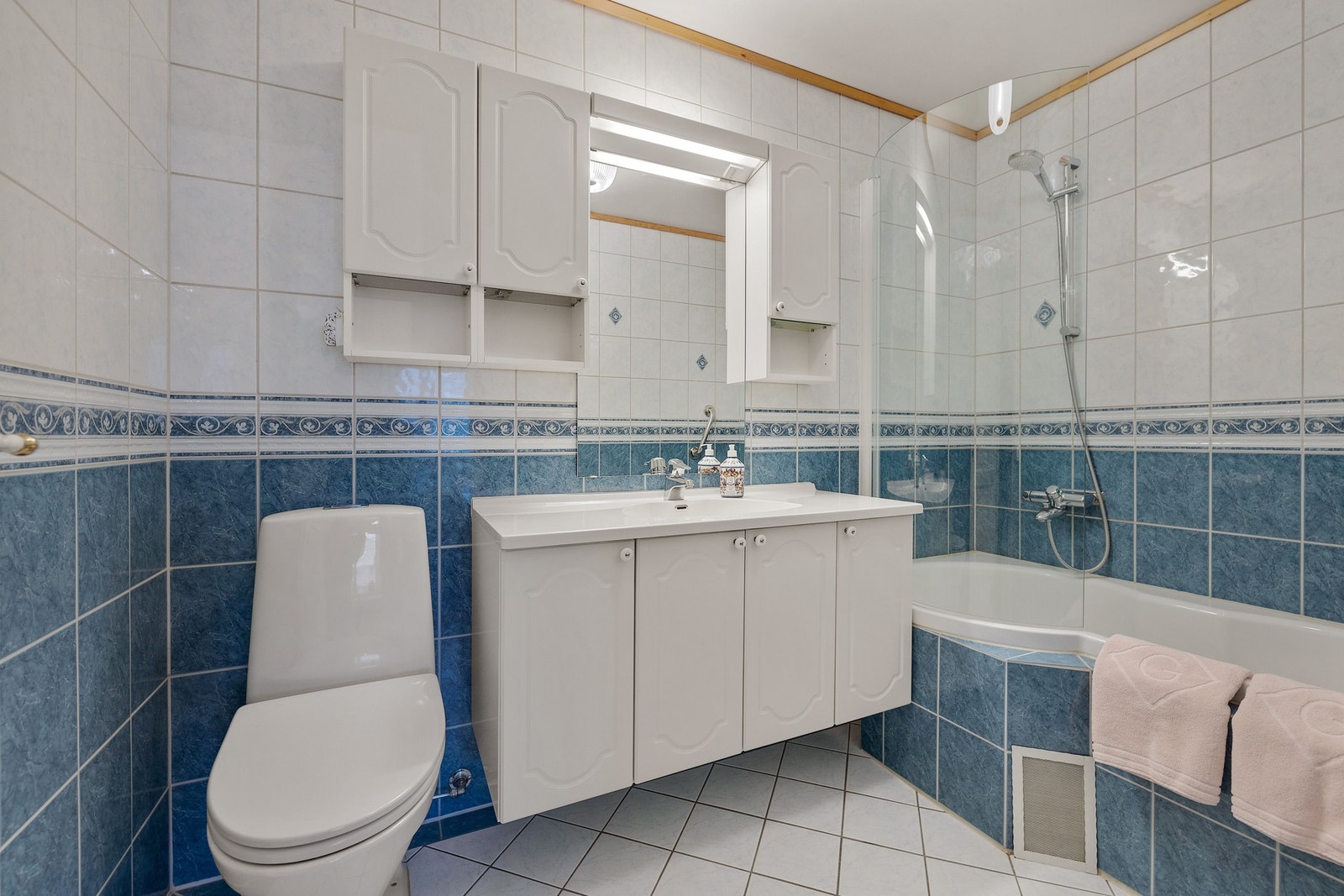 Flislagt bad med vannbåren gulvvarme, gulvstående toalett, innbygd badekar og vegghengt servant på servantskap. Galleribilde