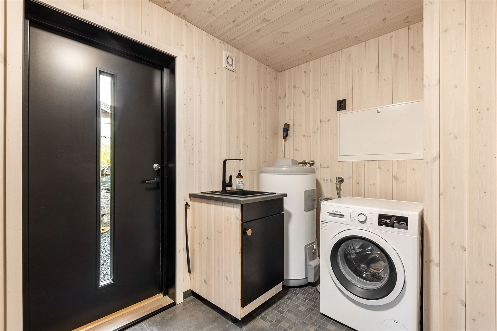 Fra entré kommer du inn på praktisk vaskerom med flis og varmekabler på gulv, lakket panel på vegger himling Galleribilde