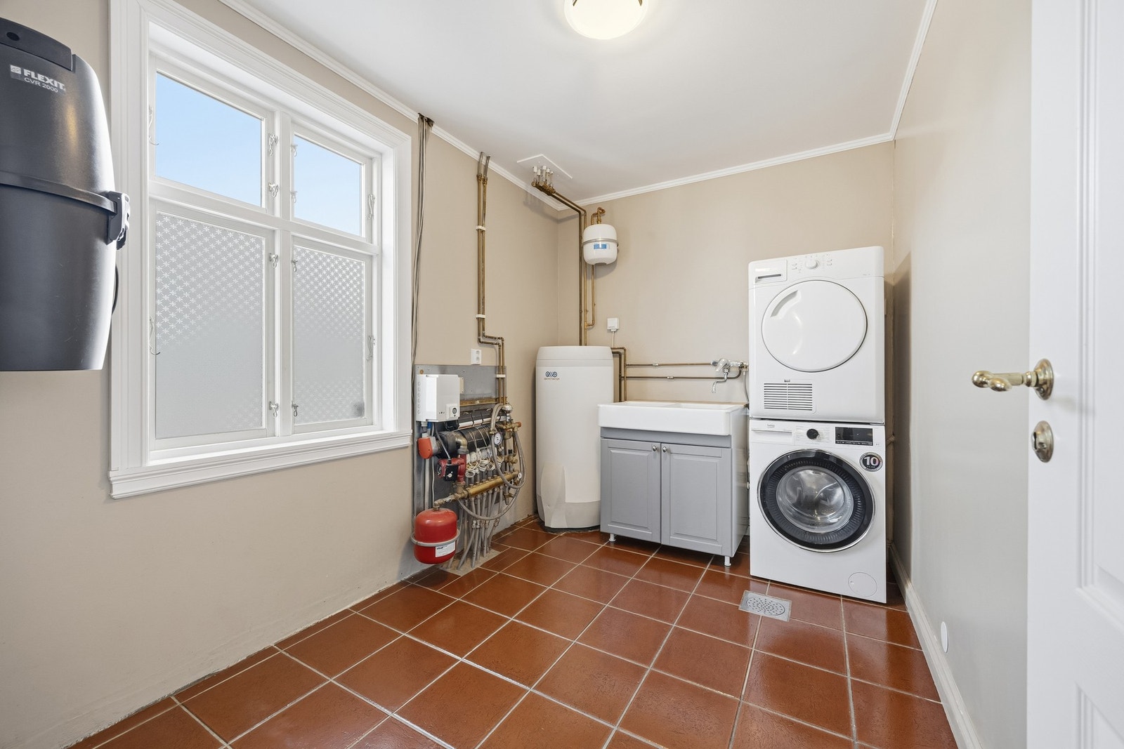 Praktisk vaskerom med flislagt gulv og malte veggflater. Rommet er utstyrt med servantinnredning (ny i 2022), opplegg for vaskemaskin og tørketrommel, samt sentralstøvsuger. Galleribilde