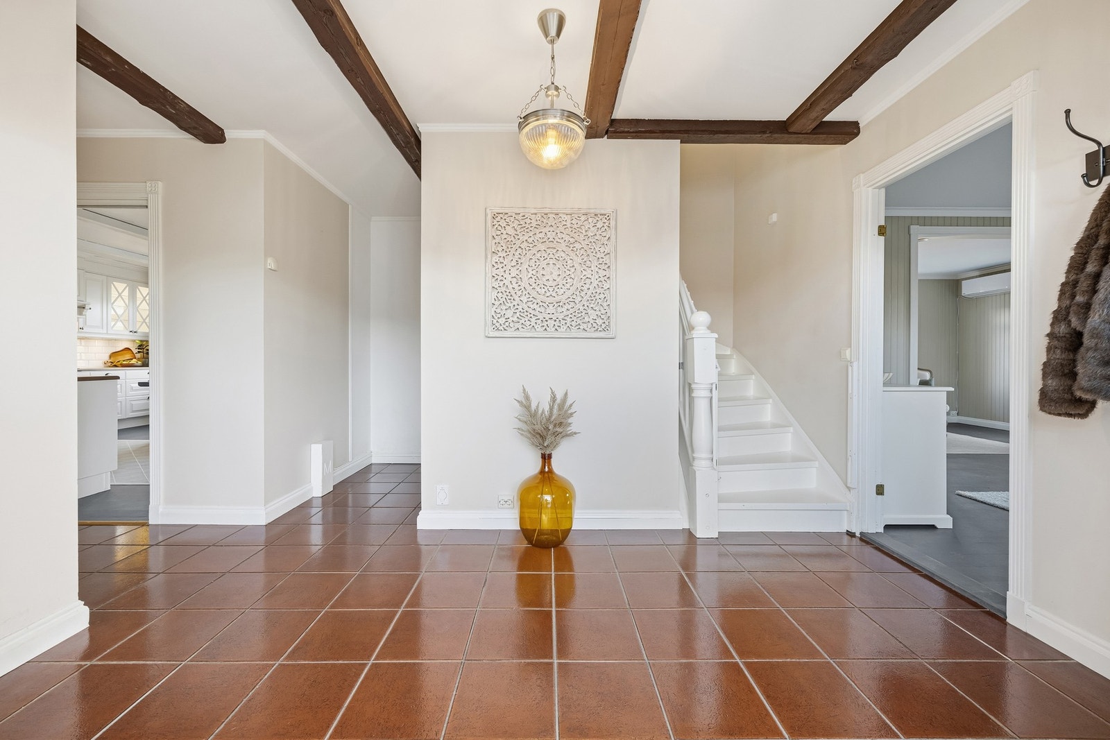 Romslig og innbydende entré med flislagt gulv med vannbåren gulvvarme og lyse, malte veggflater. Entréen fungerer som et praktisk knutepunkt i boligen, med direkte adkomst til stue, kjøkken, vaskerom og toalettrom, samt trapp opp til 2. etasje. Galleribilde