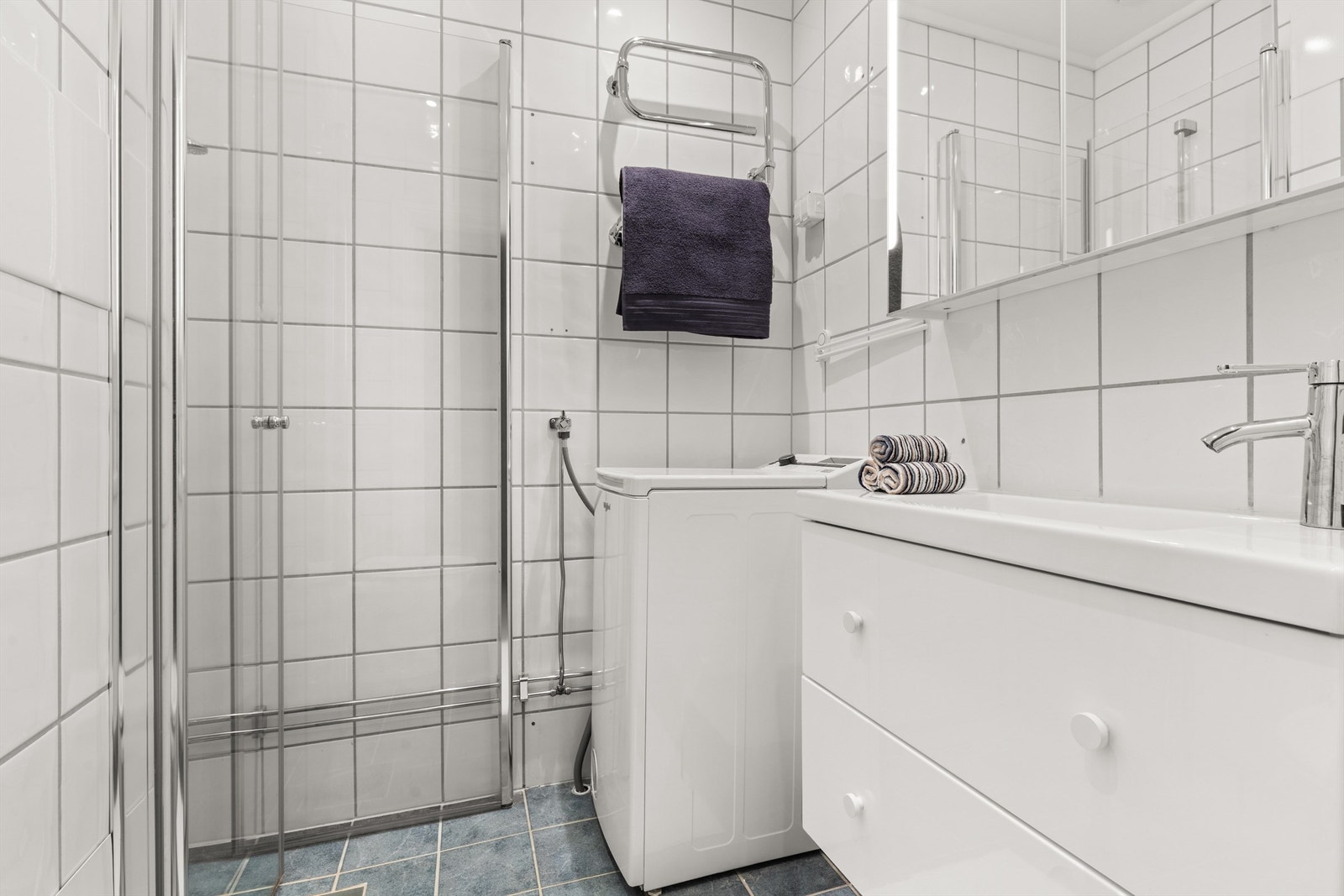 Badet er helfliset og praktisk innredet med dusjhjørne og opplegg for vaskemaskin. Galleribilde