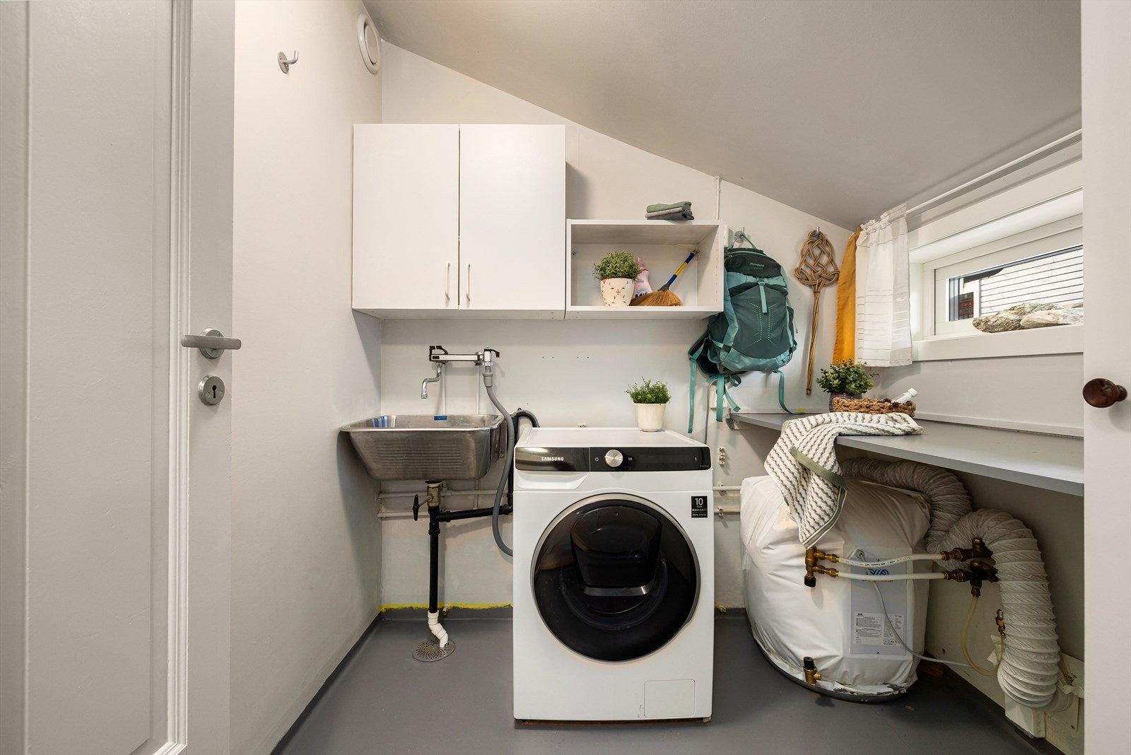 Separat og praktisk vaskerom med stålkum, møbler, varmtvannsbereder, tørkeskap og opplegg for vaskemaskin. Rommet ligger like innenfor entré Galleribilde
