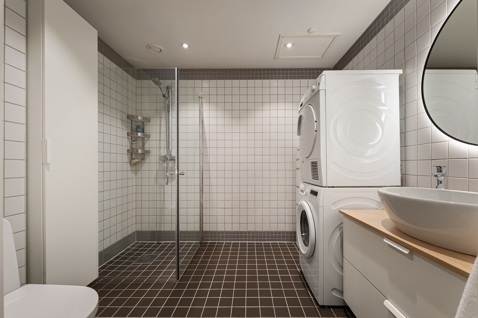 Badet er romslig og tidløst. Innredningen består av en bolleservant på servantmøbel, rundt speil med belysning, toalett og et dusjhjørne med innfellbare glassdører. Det er montert et hvitt vegghengt skap mellom dusjen og toalettet. Galleribilde