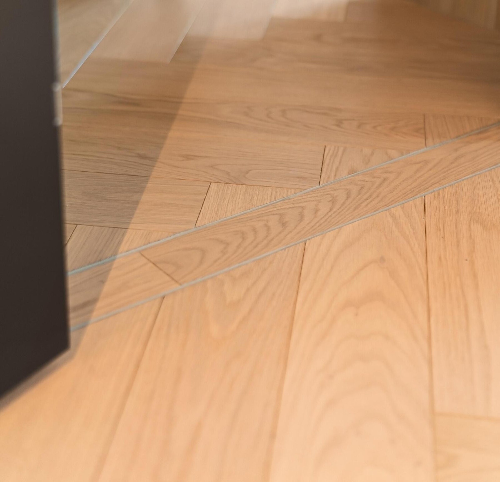 Lys fiskebensparkett i eik med nedfelte terskler. Gulvet er også lagt slik at mønsteret fortsetter på samme måte mellom rommene for en sømløs overgang. Galleribilde