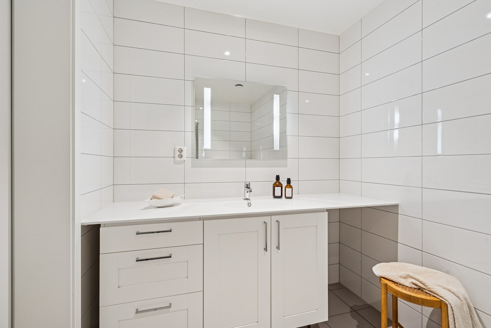 Badet er innredet med en praktisk og stilfull baderomsinnredning med skuffe- og skapseksjon og heldekkende servant som strekker seg fra vegg til vegg. Galleribilde