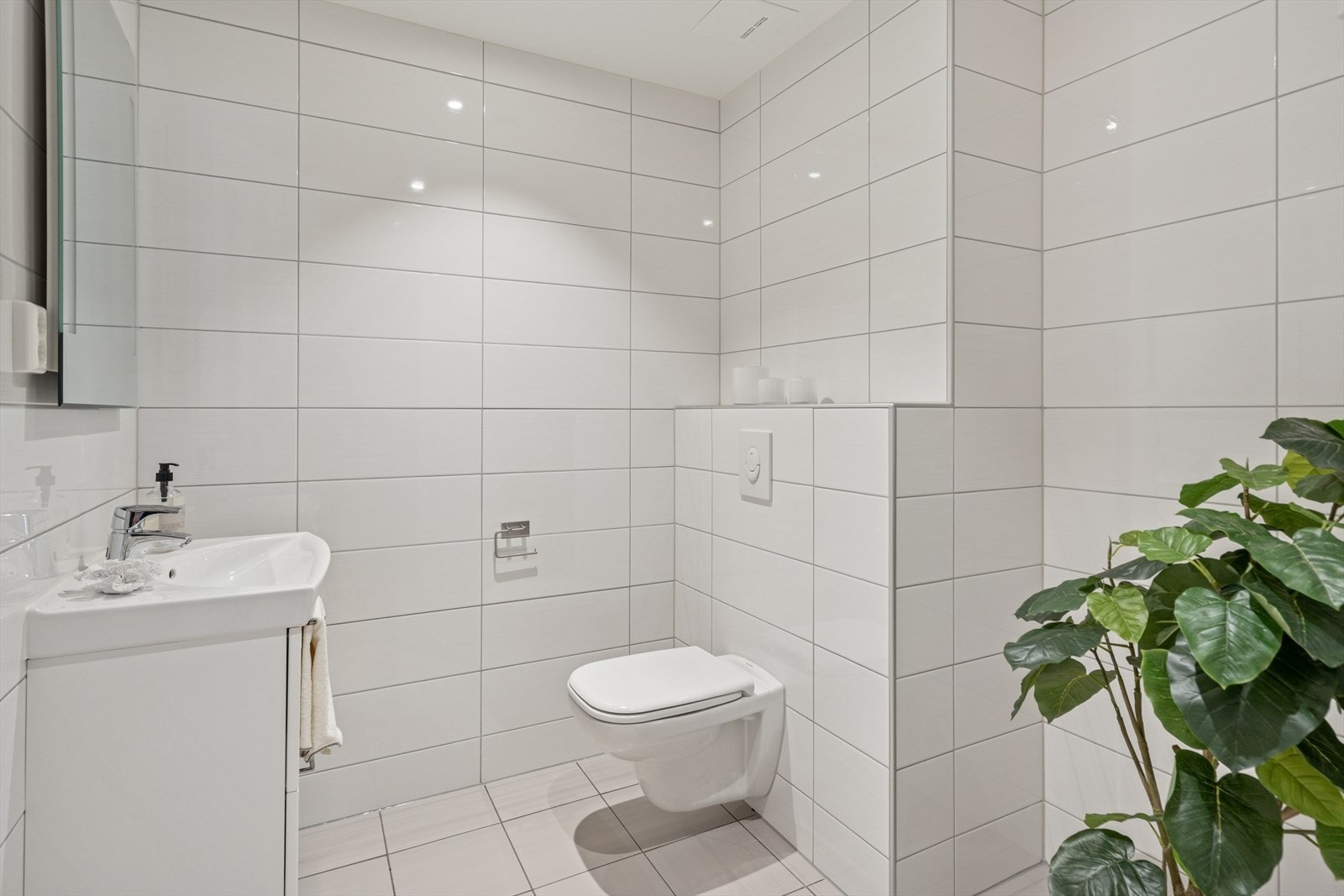 Rommet er innredet med en praktisk og stilfull baderomsinnredning med servant og skuffseksjoner, vegghengt toalett, opplegg for vaskemaskin og belyst speil. Galleribilde