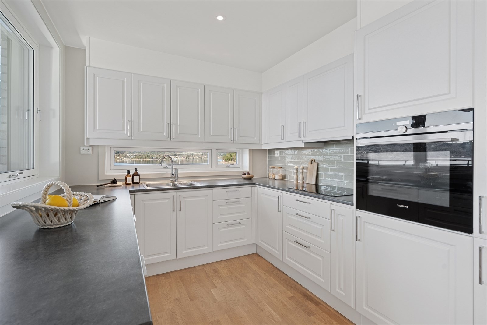 Detaljer som blant annet benkeplate i mørk utførelse med nedfelt kjøkkenservant, flislagt sone mellom benkeplate og overskap og vindu på hele 2 vegger gir kjøkkenet en komplett gjennomførelse. Galleribilde