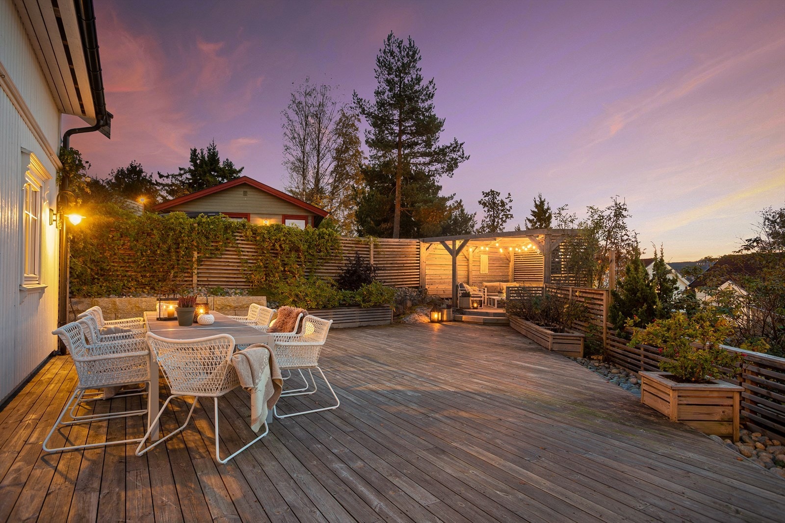 Stor, solrik terrasse med flere hyggelige sittegrupper og et pent opparbeidet bed med frodige planter og busker, perfekt for avslapping og sosiale sammenkomster. Galleribilde