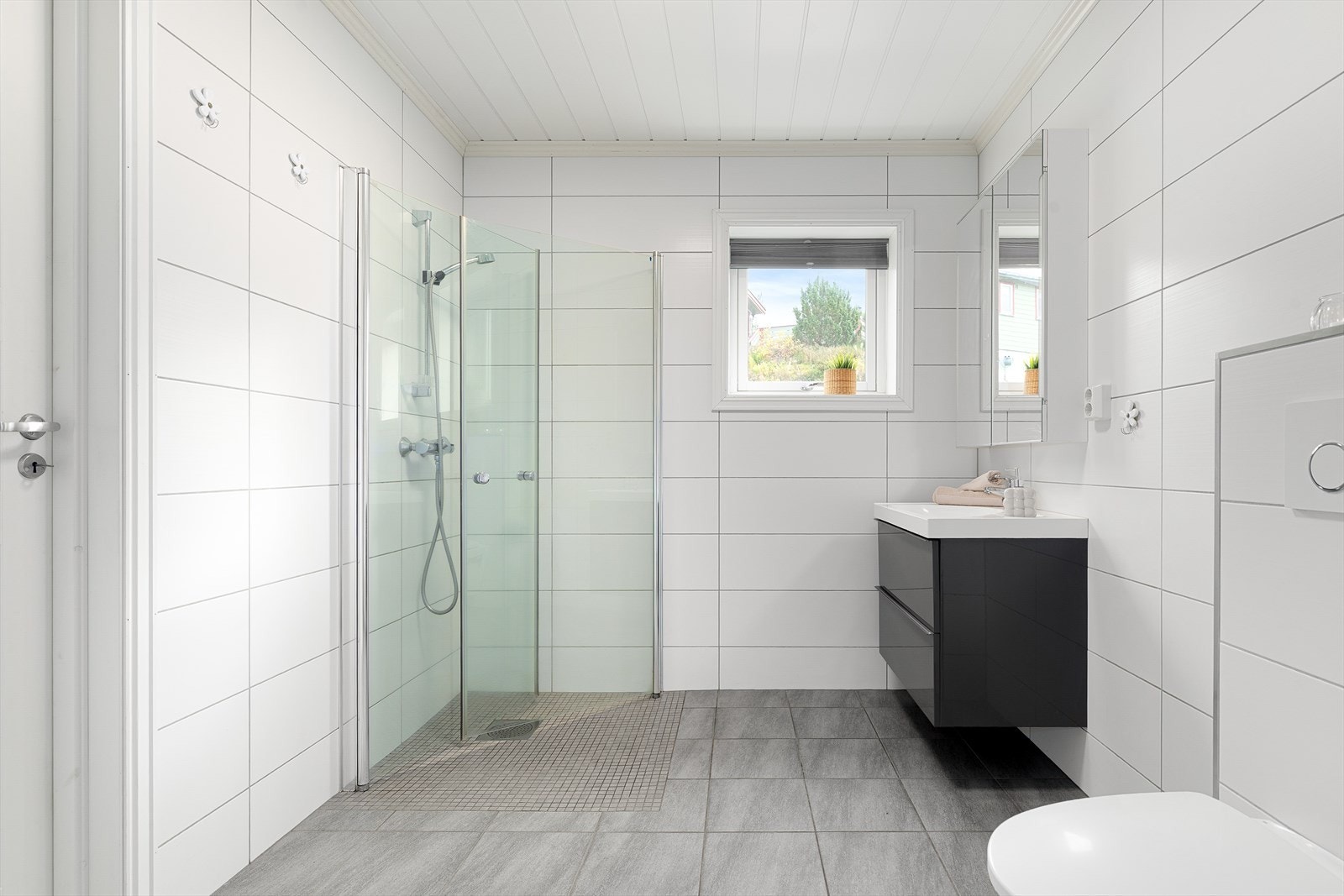 Badet i første etasje er innredet med servant med underskap, speilskap med belysning, vegghengt toalett og dusjsone med innfellbare glassdører. Galleribilde