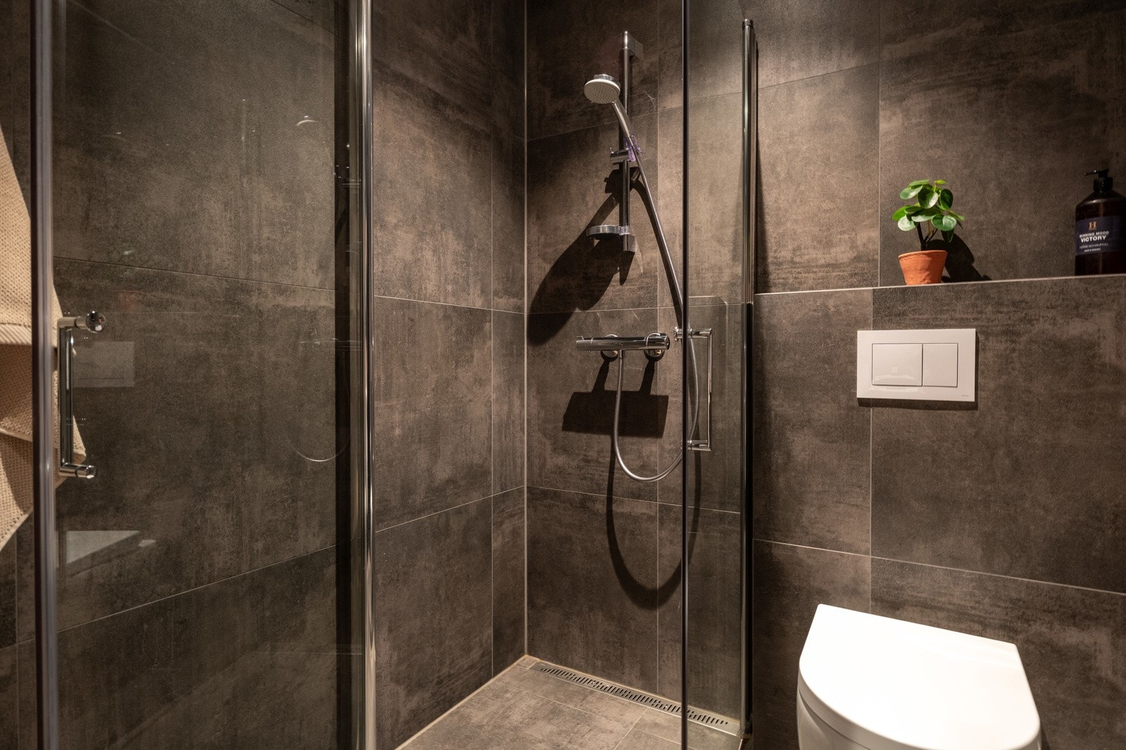 Badet har veggmontert toalett, samt dusjhjørne med innfellbare glassdører. Galleribilde