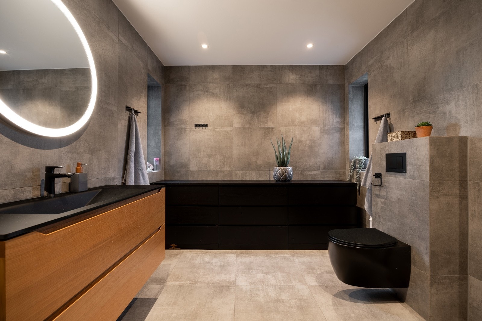 Et delikat flislagt familiebad med store gulv- og veggfliser og vannbåren gulvvvarme. Rommet er 6,7 kvm og er innredet med skuffeinnredning med nedfelt servant og veggmontert toalett. Galleribilde