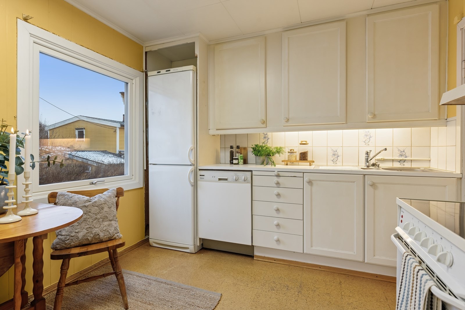 Kjøkkenet har en innredning av eldre dato med profilerte fronter, benkeplate i laminat, fliser over benk og belysning under overskap. Galleribilde